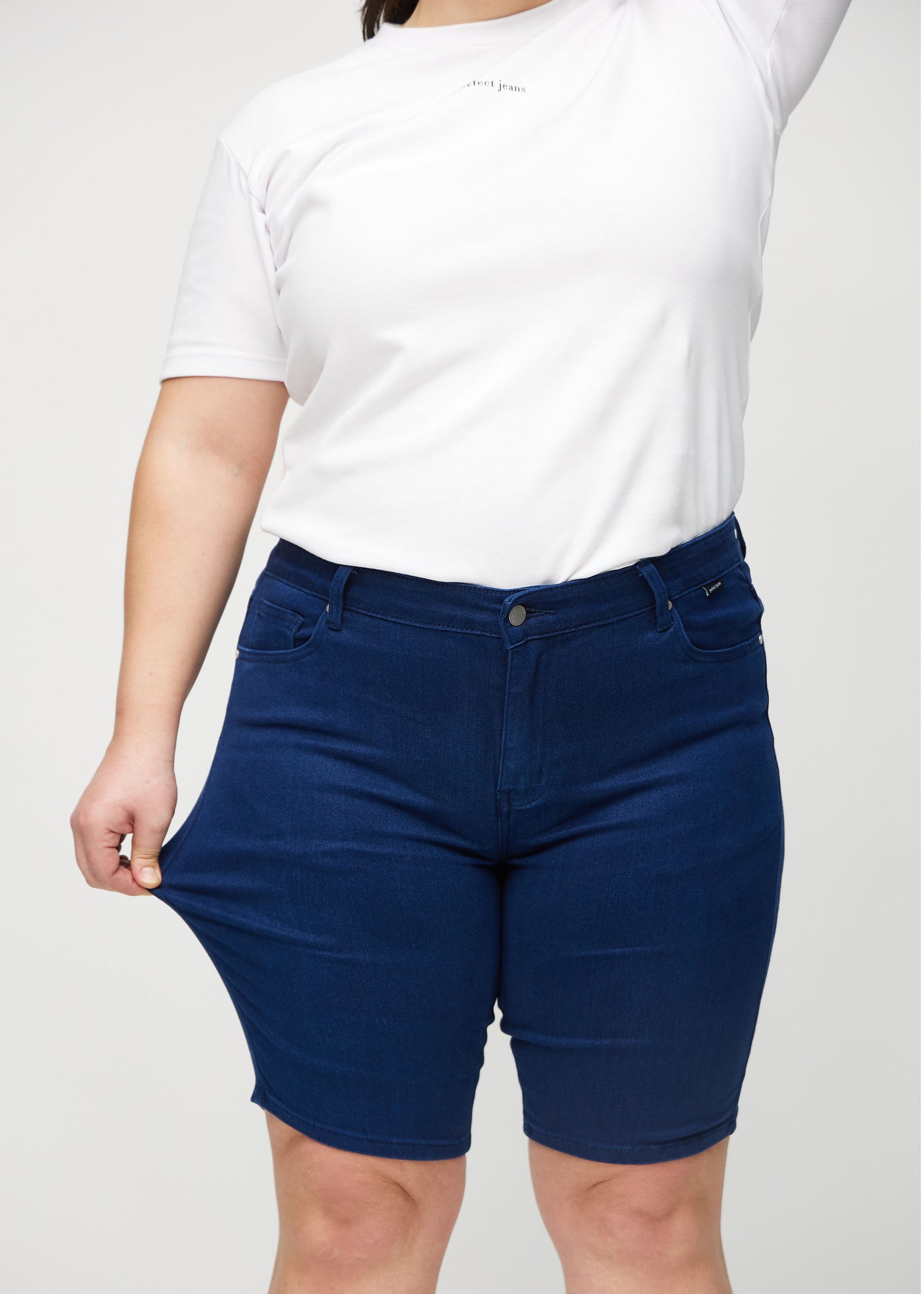 Plus-size model strækker shortsene ved låret for at vise stretch.