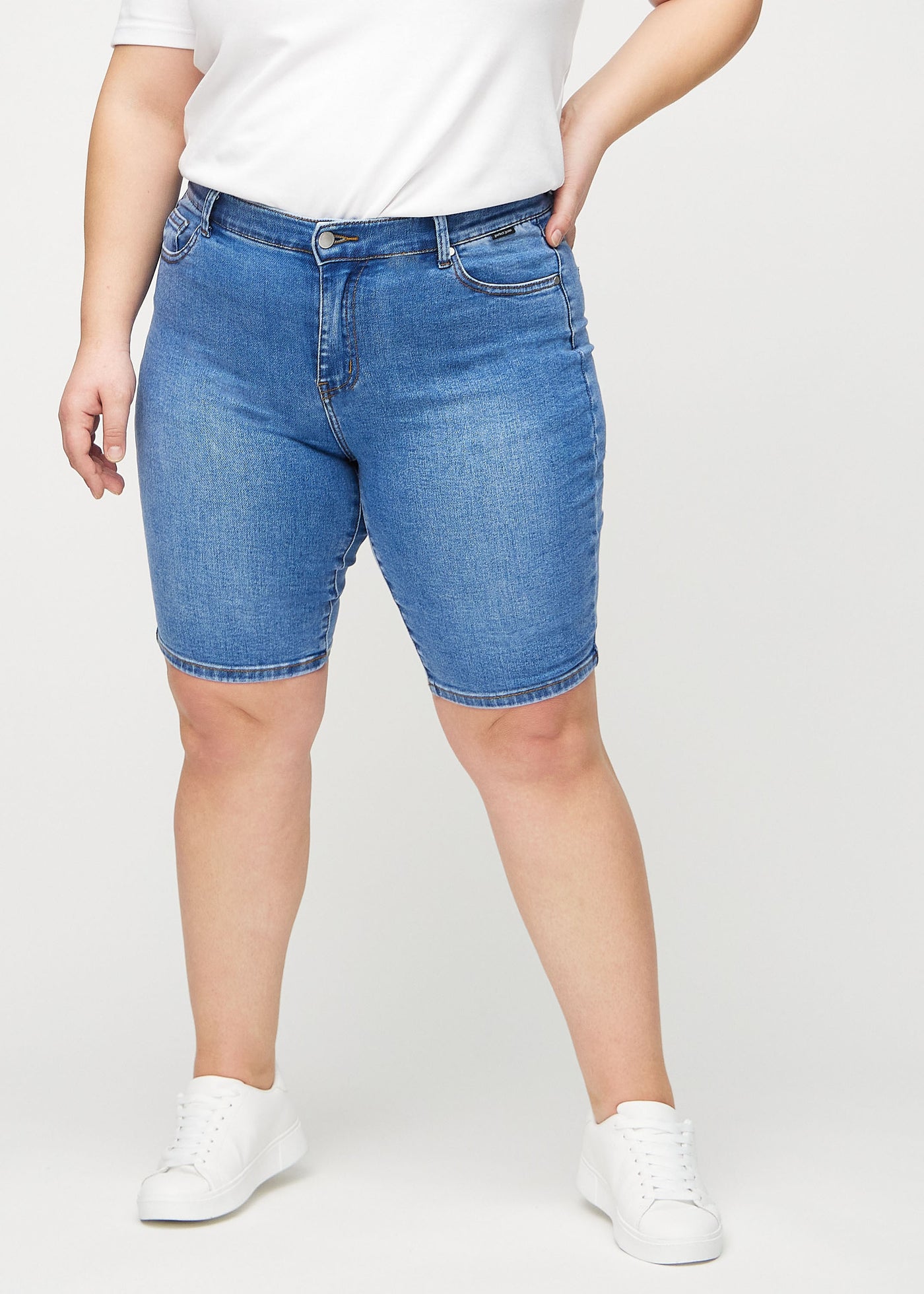 Denim skinny middle shorts, modelnavn Rivers, som sidder tæt til låret og slutter lige over knæet på en plus-size model, set forfra.