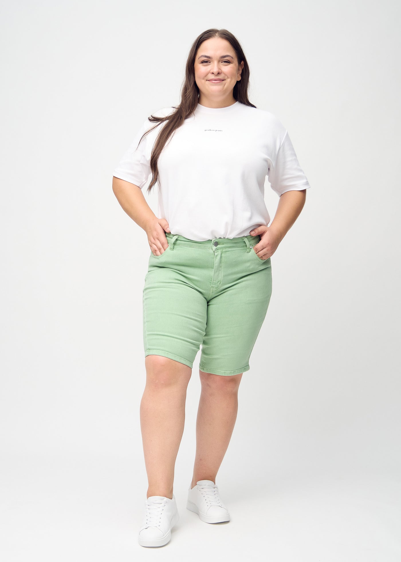 Fuldt billede af en plus-size model i lysegrønne skinny middle shorts.