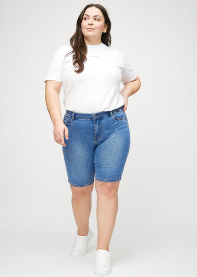 Fuldt billede af en plus-size model i denim skinny middle shorts.