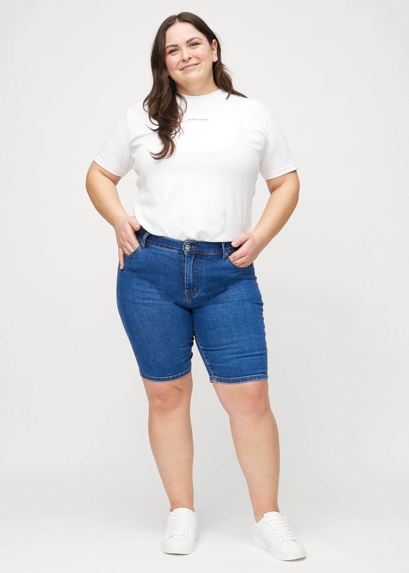 Fuldt billede af en plus-size model i mørk denim skinny middle shorts.