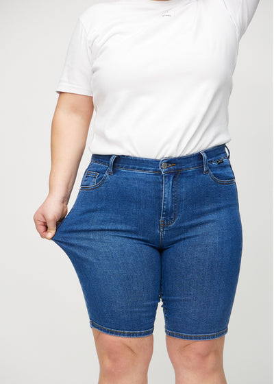 Plus-size model strækker shortsene ved låret for at vise stretch.