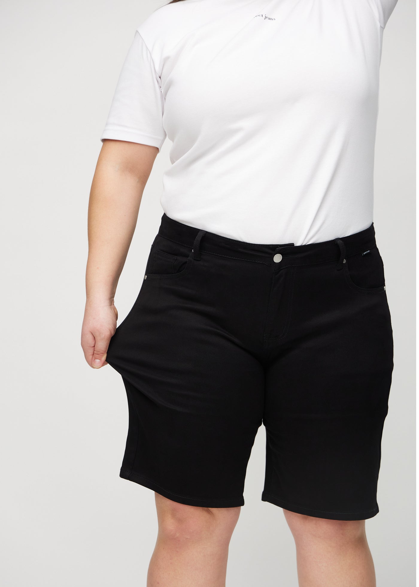 Plus-size model strækker shortsene ved låret for at vise stretch.