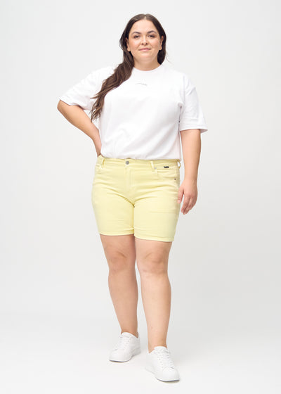 Fuldt billede af en plus-size model i lysegule skinny short shorts.