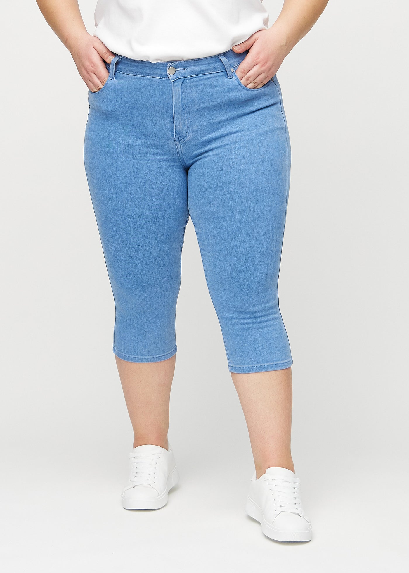 Blå skinny capris, modelnavn Geraniums, som sidder tæt til benet og slutter lige under knæet på en plus-size model, set forfra.