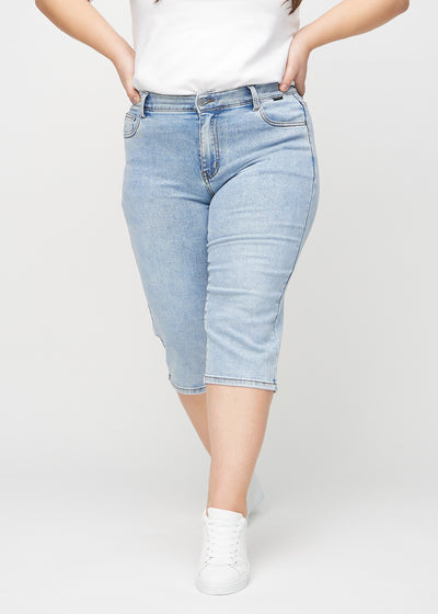 Lys denim regular capris, modelnavn Waves, som sidder lige til benet og slutter lige under knæet på en plus-size model, set forfra.