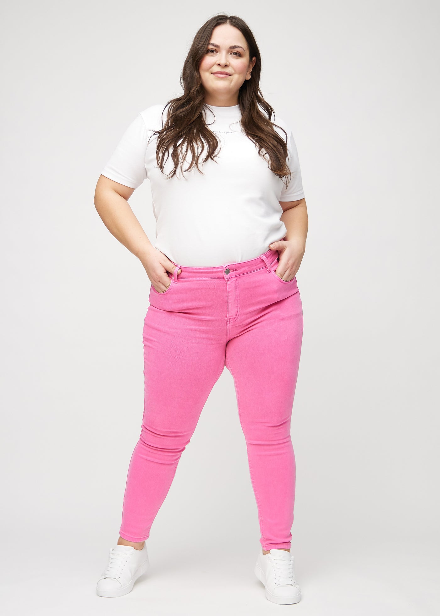 Fuldt billede af en plus-size model i lyserøde skinny jeans.