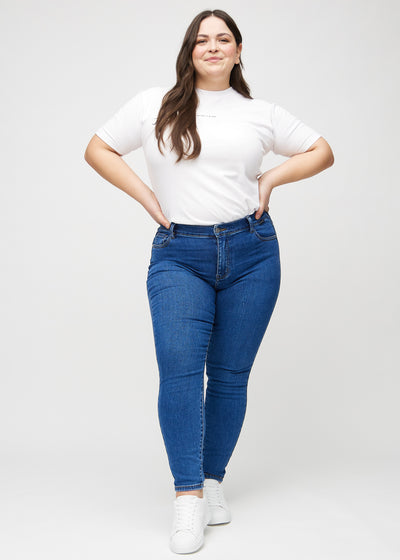 Fuldt billede af en plus-size model i mørk denim skinny jeans.