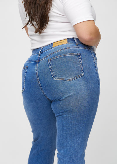 Denim slim jeans set bagfra tæt på en plus-size model for at vise detaljer.