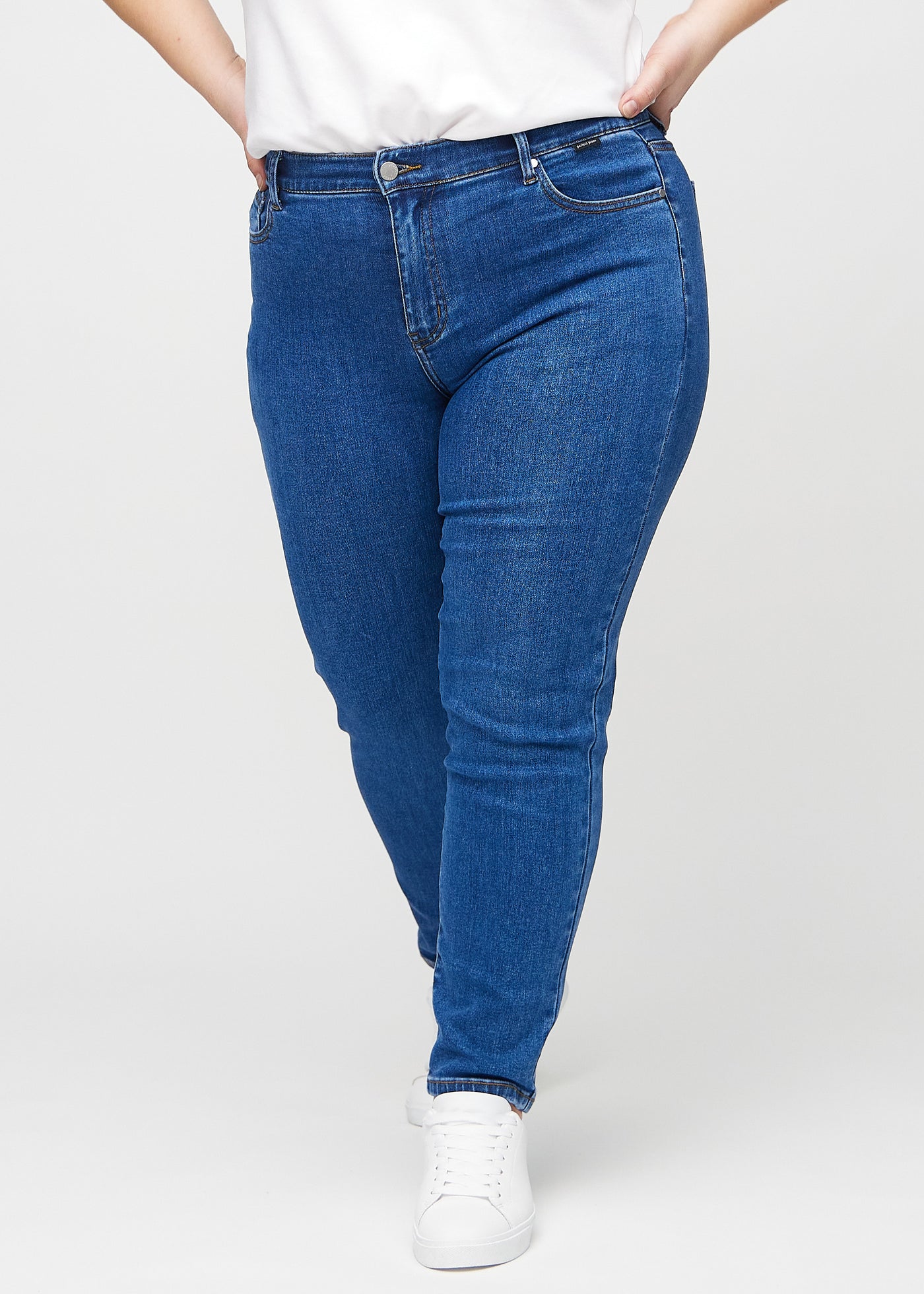 Mørk denim slim jeans, modelnavn Oceans, som sidder tæt til benet, dog lidt løsere ved anklen, på en plus-size model, set forfra.