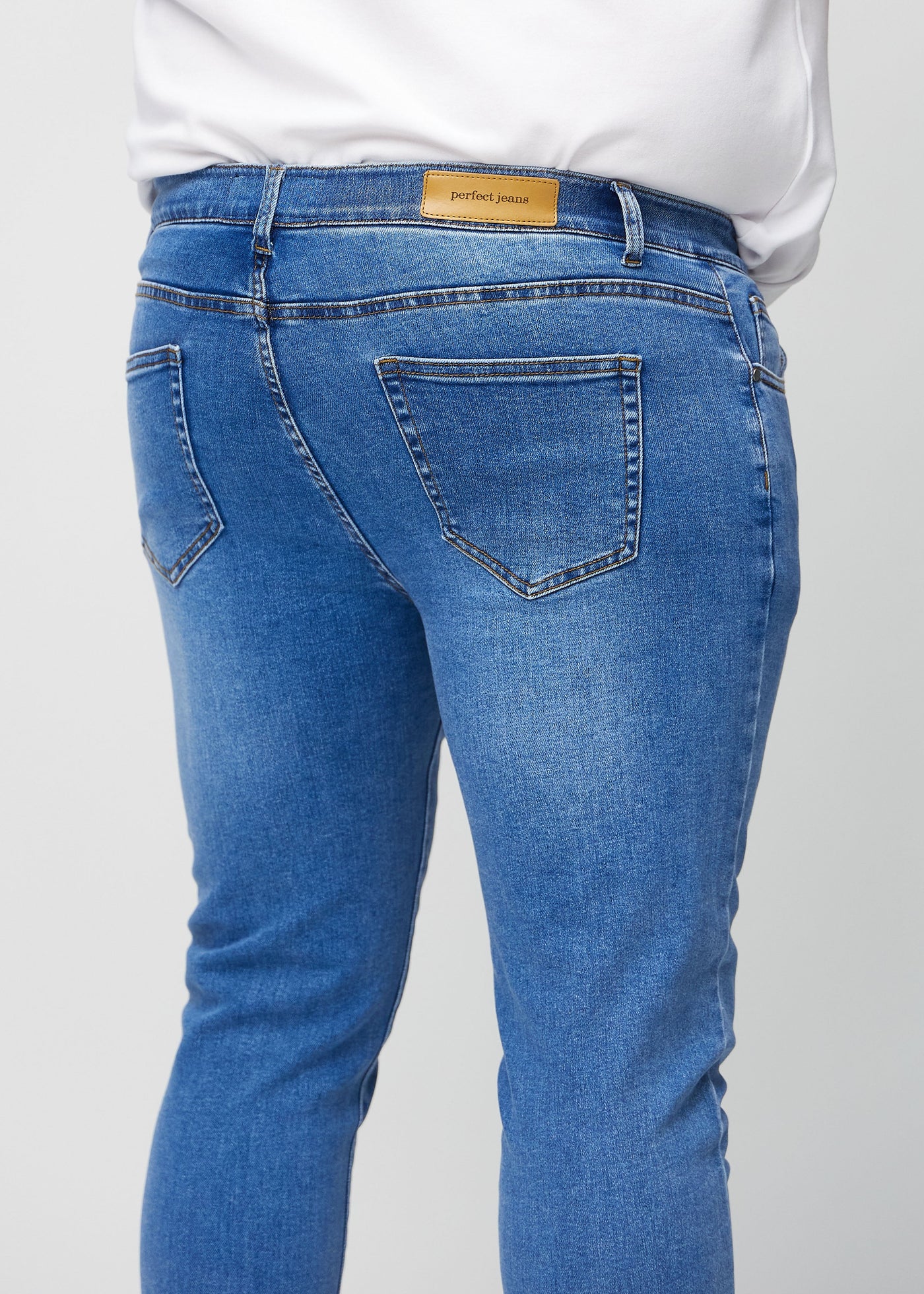 Denim slim jeans set bagfra tæt på en plus-size model for at vise detaljer.