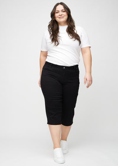 Plus-size model går ind i billedet, strækker i sine capris, viser dem frem ved at dreje rundt, og forlader derefter billedet.